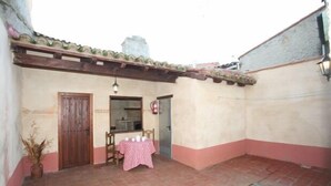 Un petit espace patio avec un sol carrelé, une porte en bois, une table recouverte d’une nappe à carreaux et un pot de fleurs.