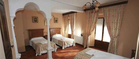 Camera d'albergo con due letti, un'ampia finestra con tende, un termosifone e un lampadario.