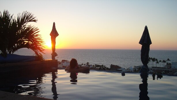 A serene pool area with a sunset view, palm trees, and a calm sea. - Downtown Penthouse-Style Apartment (Puerto Vallarta)
