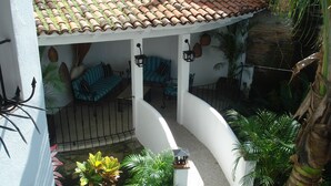 A covered outdoor seating area with chairs and tables, surrounded by potted plants and a palm tree. - Downtown Penthouse-Style Apartment (Puerto Vallarta)