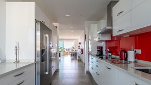 A modern kitchen with white cabinets, stainless steel appliances, and a red accent wall.