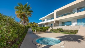 A modern building with a pool, surrounded by greenery and palm trees.