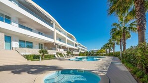 A modern hotel with a pool area, outdoor seating, and palm trees.