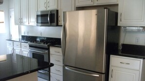 A kitchen with white cabinets, a stainless steel refrigerator, a microwave, and a stove.