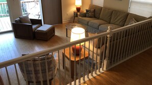 A living room with a sofa, a chair, a coffee table, and a lamp. There is a staircase with a railing leading to an upper level.