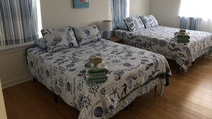 A room with two beds, each with a nautical-themed bedspread, a small painting on the wall, and a window with curtains.