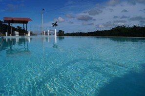 Uma piscina translúcida com um deck de madeira e uma estrutura com telhado vermelho.