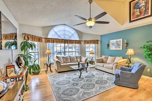 A spacious living room with a high ceiling, large windows, and a ceiling fan. - Easy Walk to Pool, Family Kids Friendly by Disney (Kissimmee)