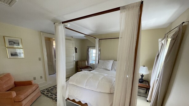 A four-poster bed with white bedding, a wooden headboard, and a small bedside table with a lamp.