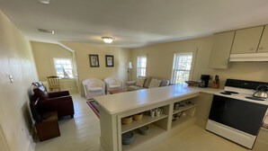 A spacious kitchen with a central island, white cabinetry, and a built-in oven. There is a dining area with a red sofa and two white armchairs.