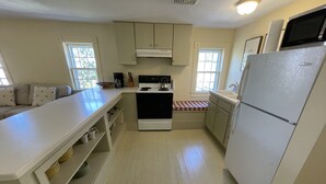 A compact kitchen with white cabinets, a stove, a refrigerator, and a window.