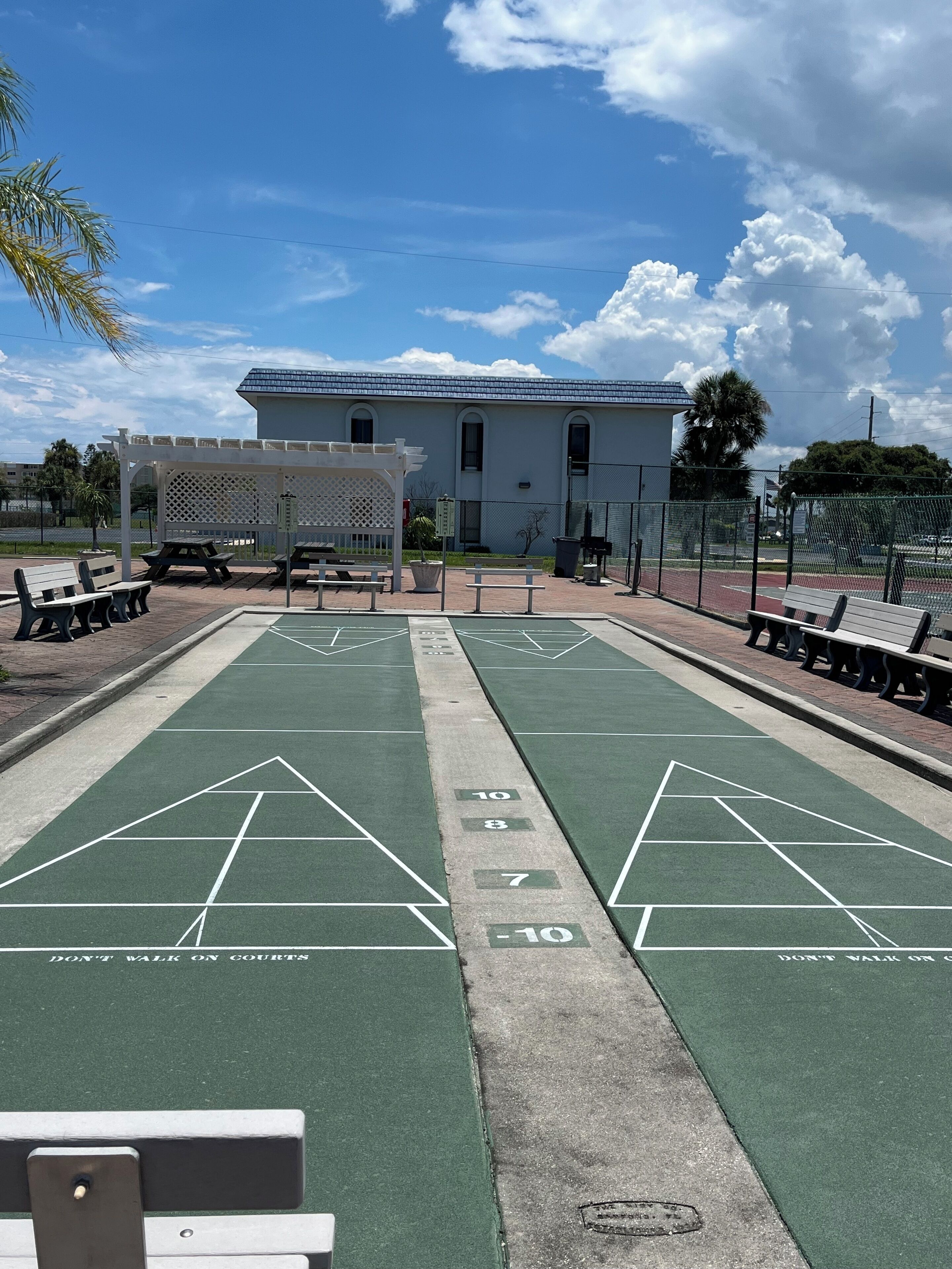 Ein Shuffleboard-Spielfeld mit Bänken und einem weißen Gebäude im Hintergrund.