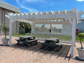 A covered outdoor seating area with picnic tables and a white lattice fence. - Ocean Front Condo on ground floor with ideal location in  Cocoa Beach. (Cocoa Beach)