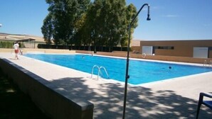 Una piscina con agua cristalina azul, rodeada por una solana empedrada y árboles.
