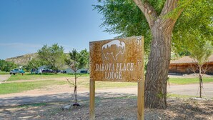 A rustic wooden sign for Dakota Place Lodge with a bison silhouette, surrounded by trees and a clear sky. - Badlands Suite of Dakota Place Lodge in Medora! (Medora)