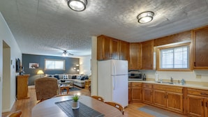 A modern kitchen with wooden cabinets, a white refrigerator, and a dining area with a round table and chairs. - Badlands Suite of Dakota Place Lodge in Medora! (Medora)