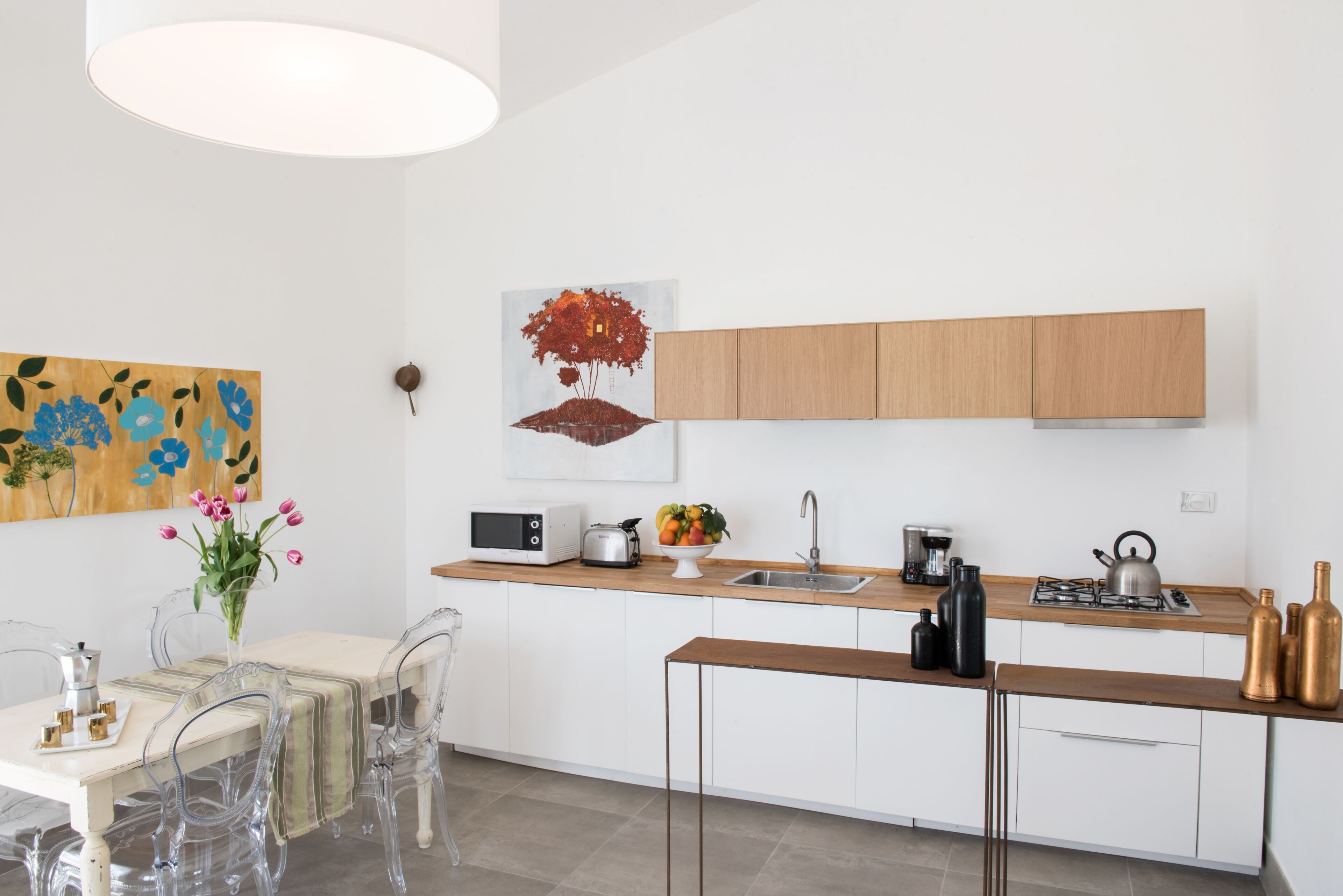 Une cuisine moderne avec des meubles blancs, un plan de travail en bois, un four à micro-ondes, une bouilloire et un évier.