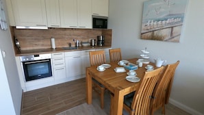 A modern kitchen with white cabinets, a wooden countertop, and a dining area with a wooden table and chairs.