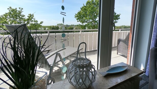 A balcony with a glass door, a wicker chair, a table with a decorative fish plate, and a potted plant.