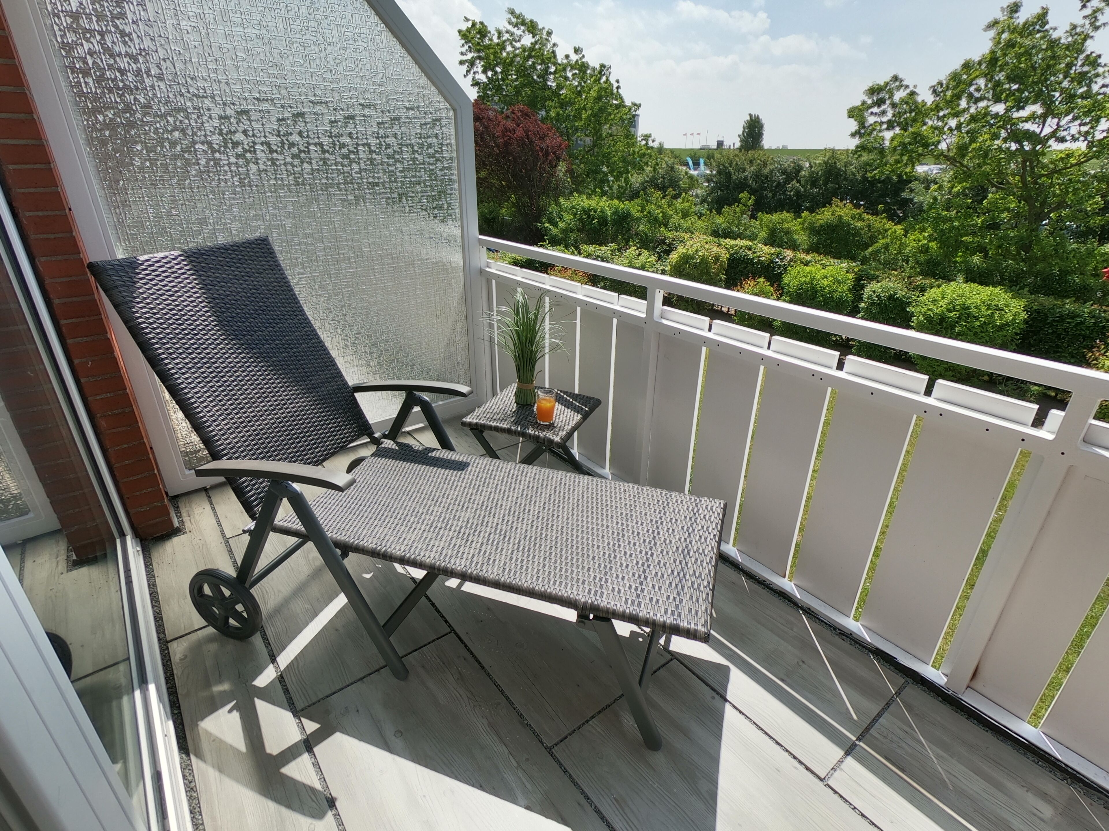 Ein Balkon mit zwei schwarzen Stühlen, einem kleinen Tisch, einem Topfpflanzen und einem Glas Orangensaft.