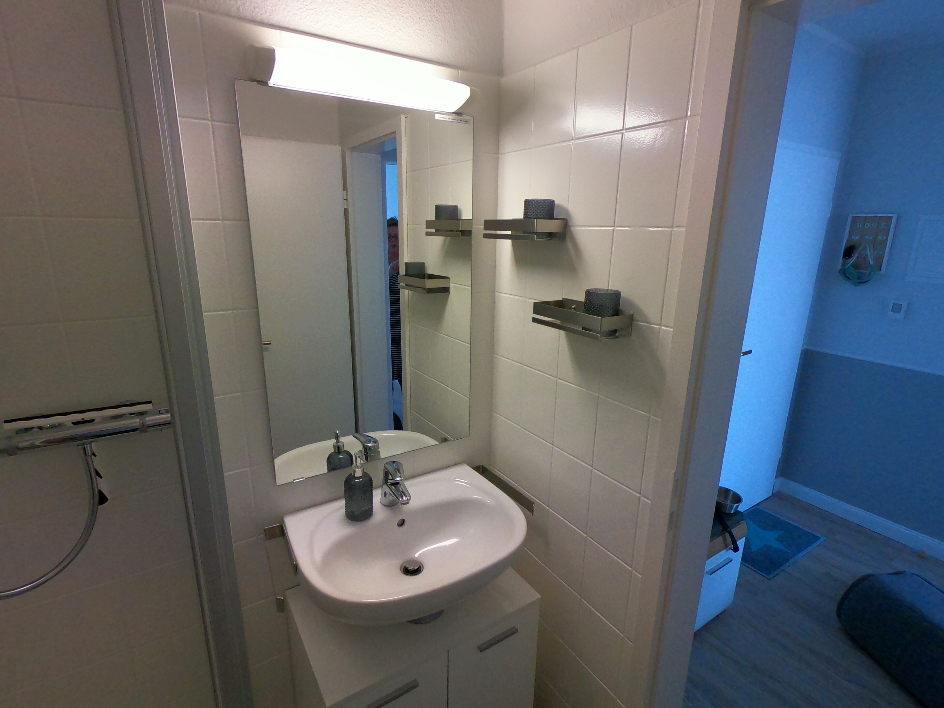 Een badkamer met een wit wastafelmeubel, spiegel en twee handdoekhouders aan de muur.