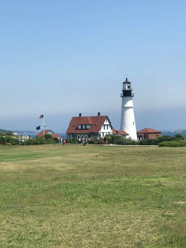 A lighthouse with a white exterior and a red roof, adjacent to a building with a similar red roof.