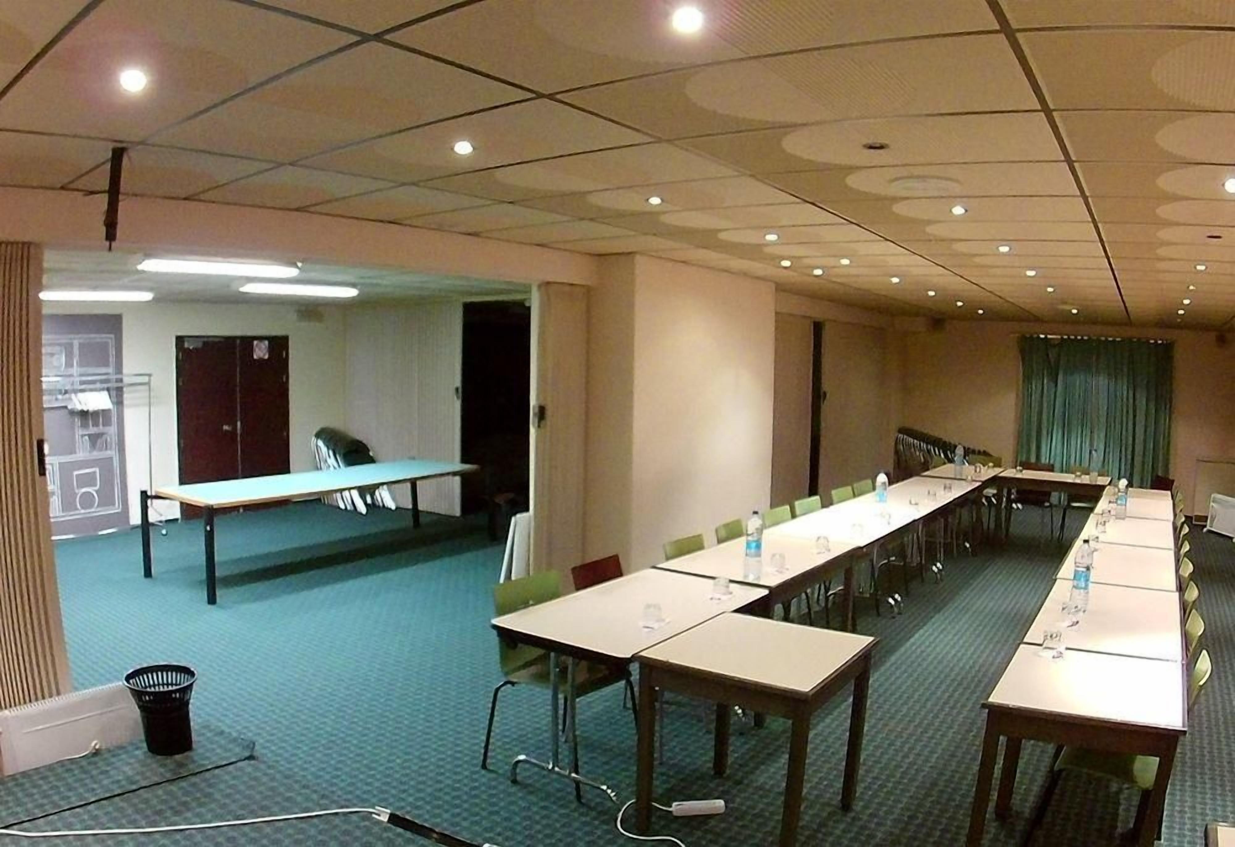 Ein Konferenzraum mit langen Tischen, Stühlen und einer Projektionsleinwand.