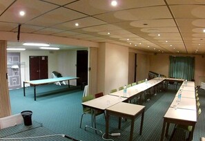 Un salón de conferencias con mesas largas, sillas y una pantalla para proyector.