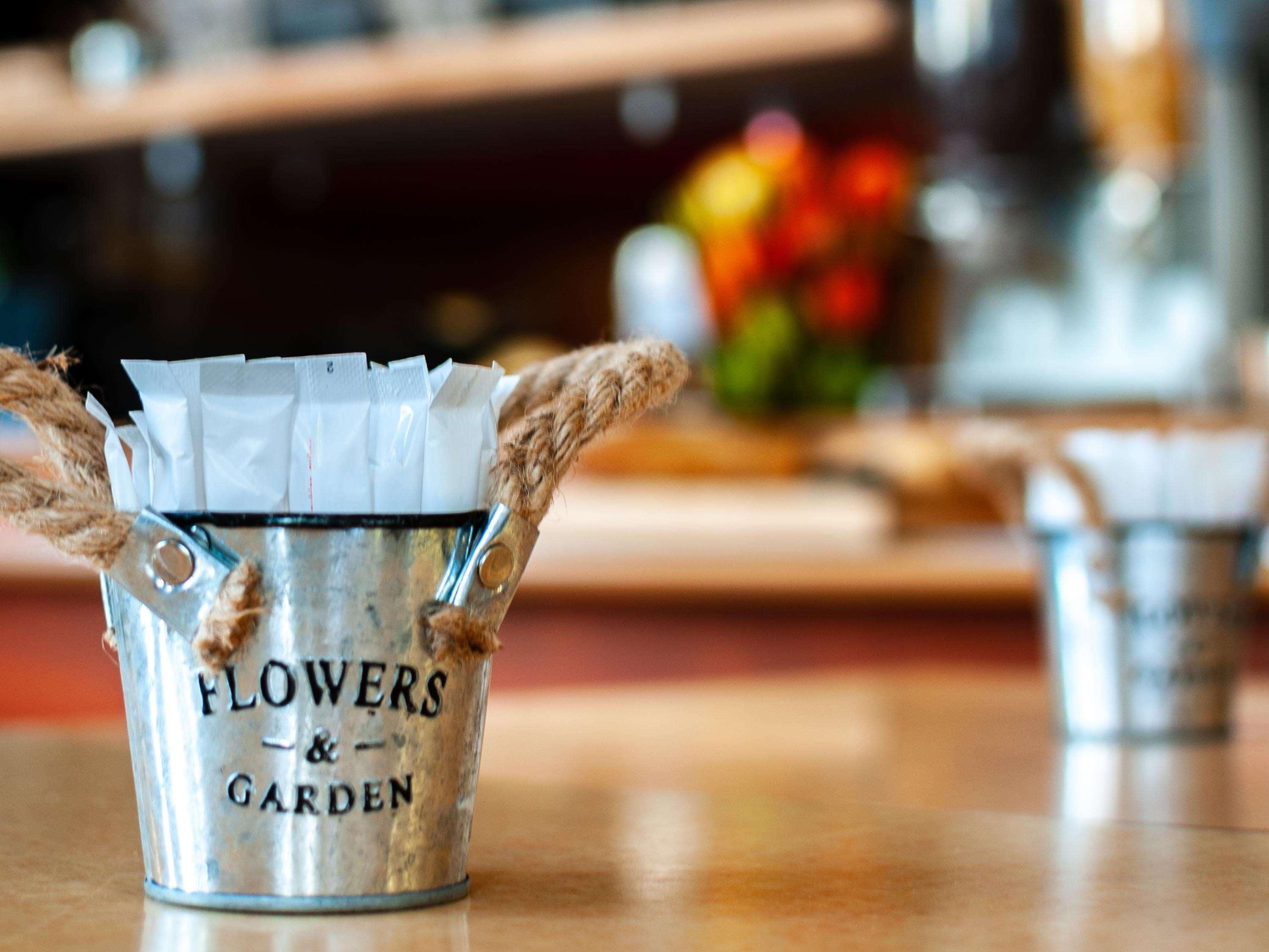 En metalspand med håndtag i reb, mærket 'FLOWERS & GARDEN', placeret på en træoverflade.
