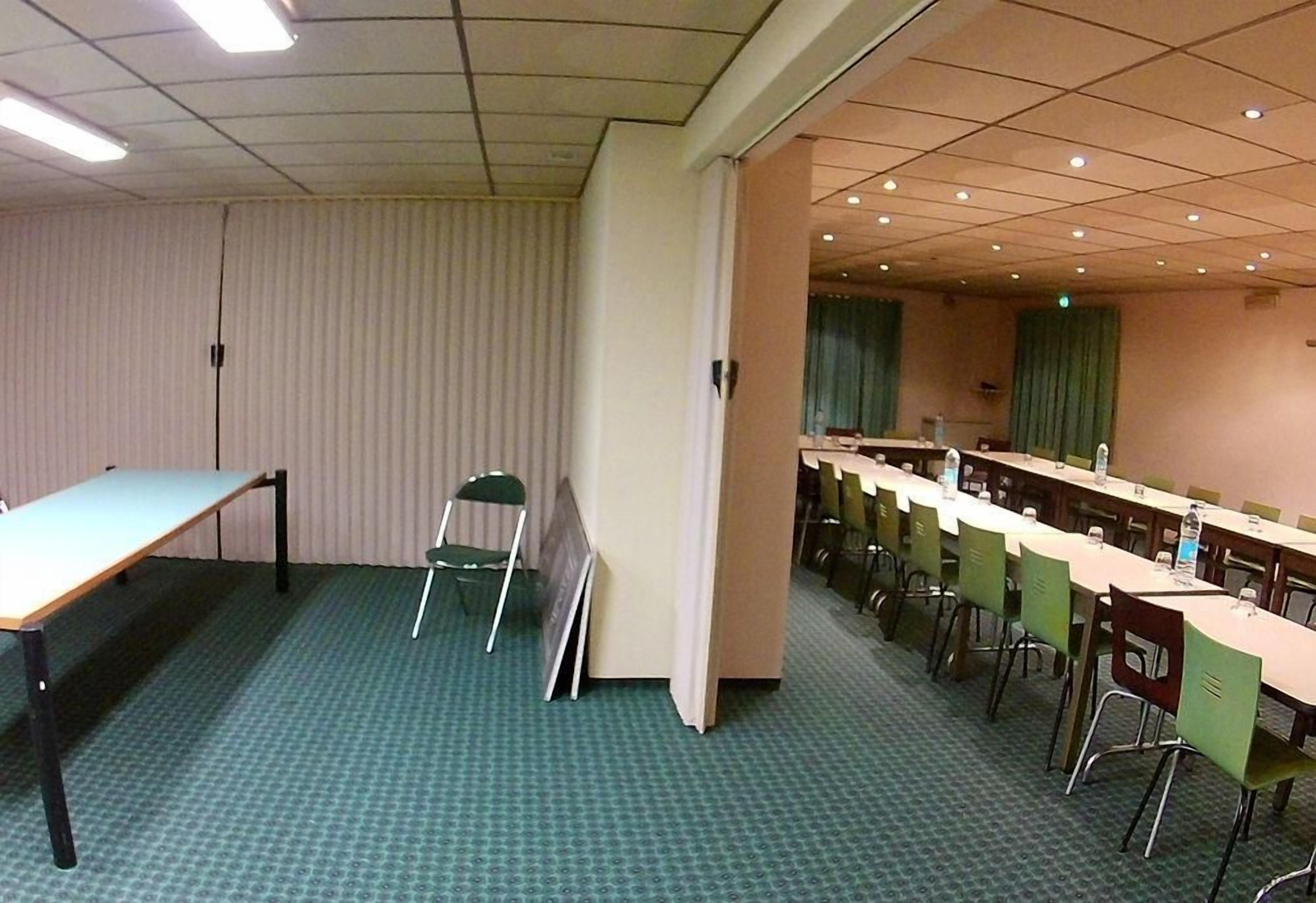 Un salón de conferencias con una larga mesa, sillas, una pantalla de proyector y piso alfombrado.