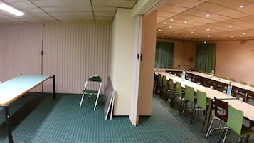Un salón de conferencias con una larga mesa, sillas, una pantalla de proyector y piso alfombrado.
