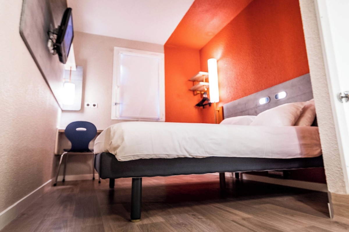 A modern hotel room with a bed, a desk, and a chair.