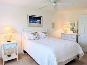 A bedroom with a bed, nightstands, a ceiling fan, a framed picture, a dresser, and a mirror.