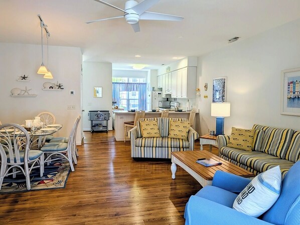 A spacious living area with a dining table, sofas, a kitchen in the background, and a ceiling fan.