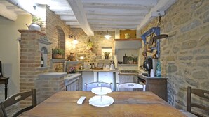 Una rústica cocina de piedra con una mesa de comedor de madera, sillas y una lámpara colgante.