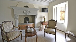 Una habitación con chimenea, dos sillones decorativos, una mesita con bandeja y un televisor en la pared.
