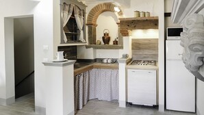 Una cocina compacta con estufa a gas, horno integrado y refrigerador. Hay un lavamanos pequeño y una ventana con cortinas.