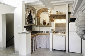 A compact kitchen with a gas stove, a built-in oven, and a refrigerator. There is a small sink and a window with curtains.