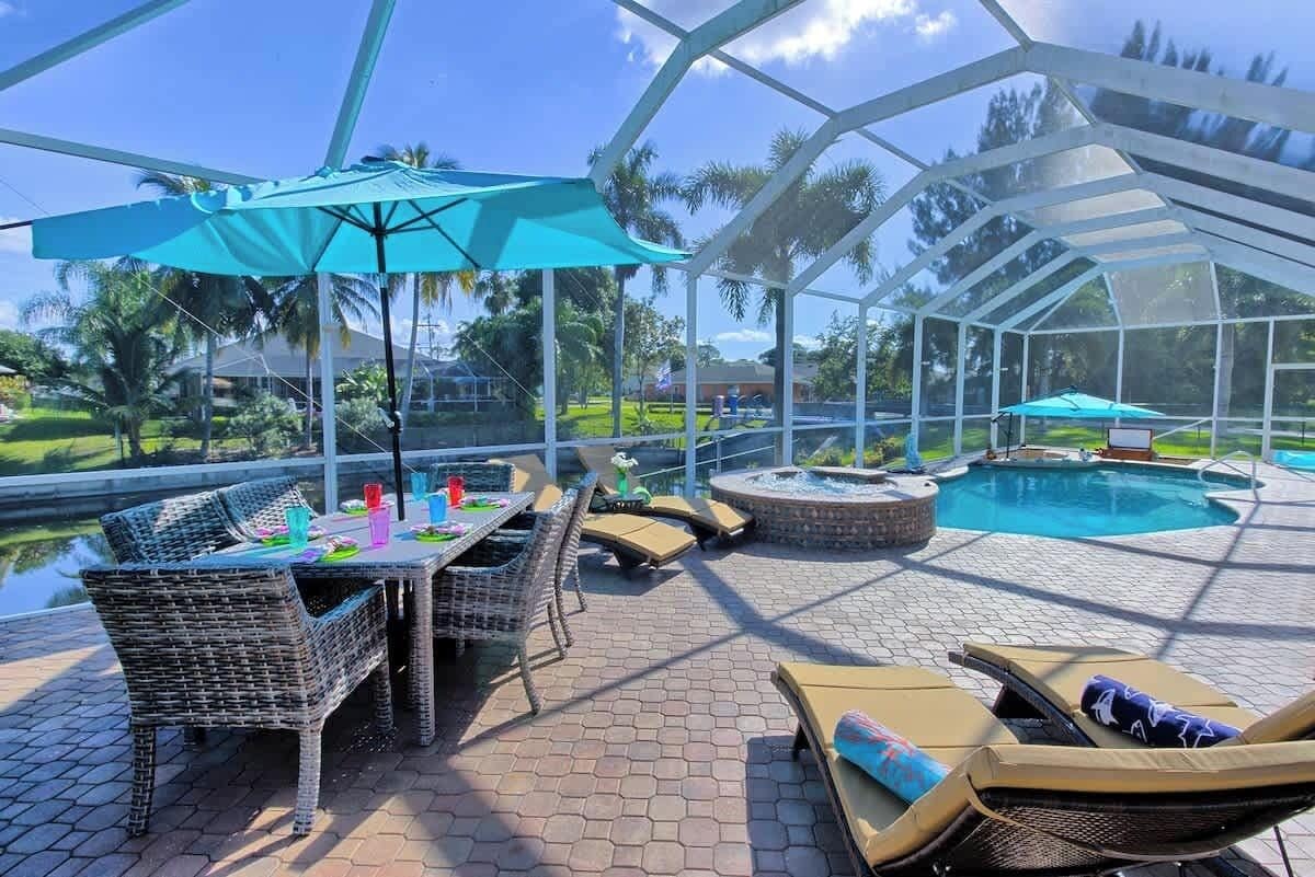 A covered outdoor area with a pool, lounge chairs, and a table with chairs.
