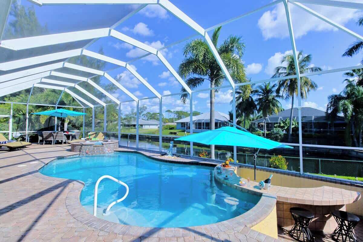 A covered outdoor swimming pool with a clear sky, palm trees, and a bar area.
