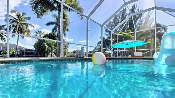 Une piscine à l’eau claire, un ballon de plage et un parasol bleu.