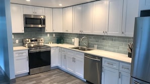 A modern kitchen with white cabinets, stainless steel appliances, and a gray backsplash.