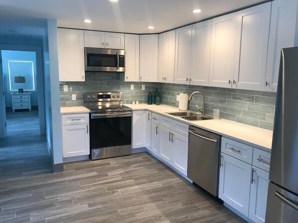 A modern kitchen with white cabinets, stainless steel appliances, and a grey tiled backsplash. - Beach front1 bedroom with pool (Georgetown)