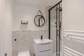 A bathroom with a white sink, a mirror, a towel rack, and a shower area. - 1-bed Flat by Oxford Circus · Fitzrovia · Sleeps 4 (London)