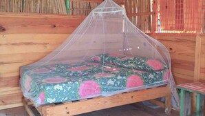 A wooden bed with a mosquito net, a patterned bedspread, and a small stool. - Private Ocean-Front Cabin with private bathroom on San Blas Island (Narganá)
