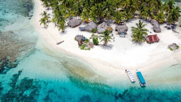 An aerial view of a tropical island with thatched-roof huts and palm trees. - Private Ocean-Front Cabin with private bathroom on San Blas Island (Narganá)