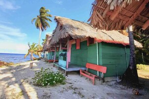 Una cabaña frente al mar con techo de paja, una banca y un pequeño porche.