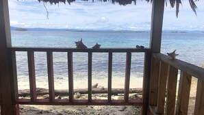 A wooden deck with a railing overlooking a beach with clear blue water and distant islands. - Private Ocean-Front Cabin with private bathroom on San Blas Island (Narganá)