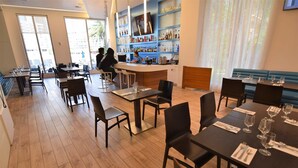 A restaurant with wooden flooring, black tables and chairs, a bar area with shelves of bottles, and large windows allowing natural light. - Bw-1208b (Hallandale Beach)
