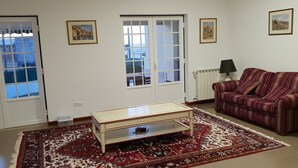 A living room with a sofa, a coffee table, a patterned rug, and two windows with curtains. - Harmonic House with sea view (Atalaia Lourinhã)